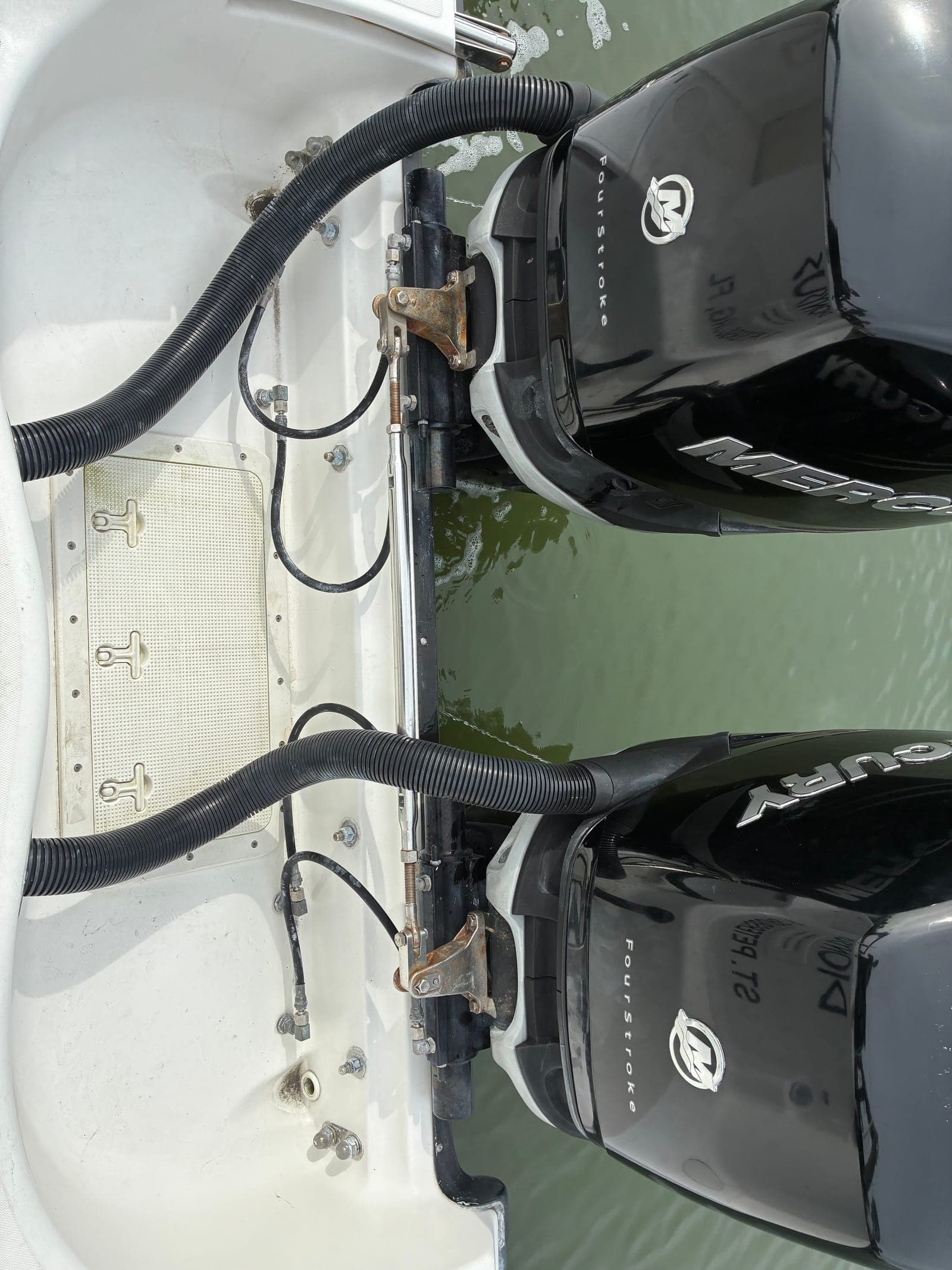 Close-up of twin Mercury powerheads with cowlings off during a 100-hour service, showing the fuel and electrical systems the checklist covers