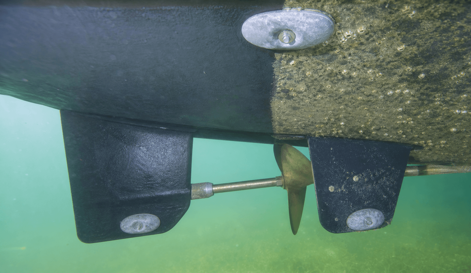 Underwater view of a boat hull and running gear showing cleaned antifouling paint beside light marine growth